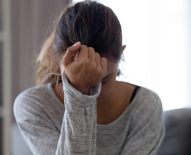A young woman in distress holding her fist to her forehead.